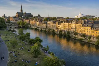 Panoramic summer view of Metz with historic architecture, riverbanks, and lively outdoor activity.