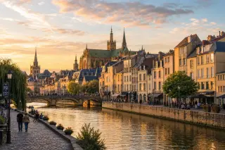 Panoramic view of Metz at sunset with the Moselle River, mixed historical and modern buildings, and people walking along the riverside.